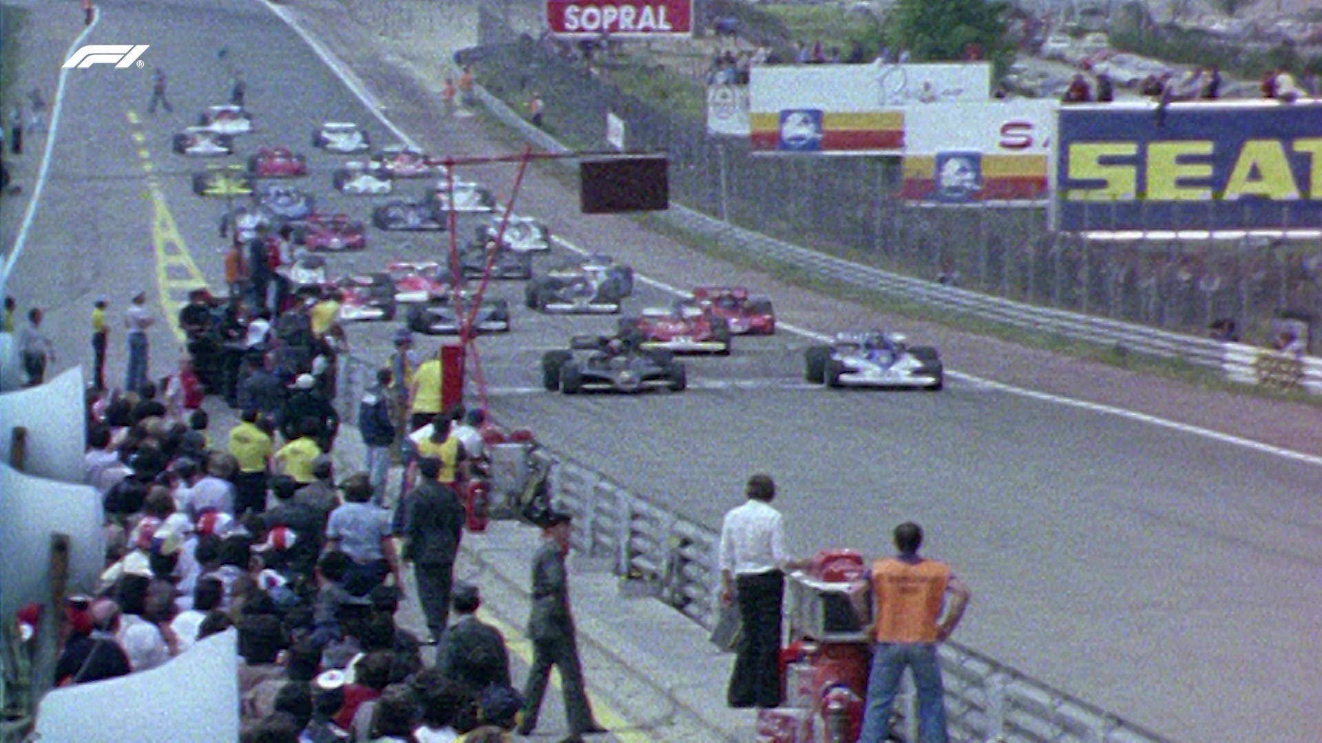 Salida de una carrera de Fórmula 1 con varios coches en parrilla y público junto al pit lane.